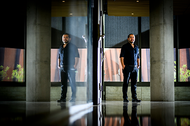 Safa Jamali standing in front of windows. He has a reflection in a glass wall on the left of the image 