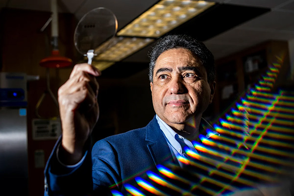 Ahmed Busnaina, WL Smith Chair and University Distinguished Professor, Mechanical and Industrial Engineering, in a lab looking at a clear round disk.