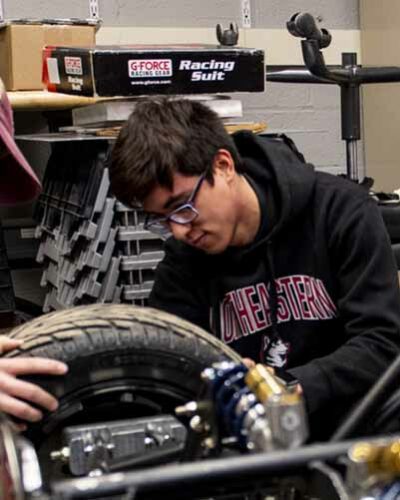 student putting tire on Baja car