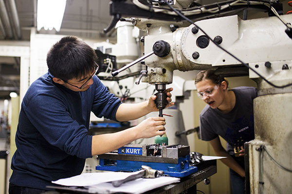 two students working with machine holding drill while looking at material that the drill is going into